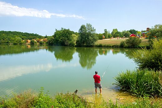 Homme pêchant dans un lac calme entouré de verdure au camping CAPFUN Ullule à Tournon d'Agenais (47).
