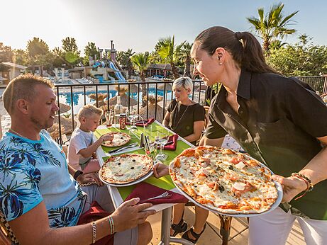 Famille mangeant pizzas au restaurant, vue piscine, camping CAPFUN Mer et Soleil à Cap d'Agde (34).